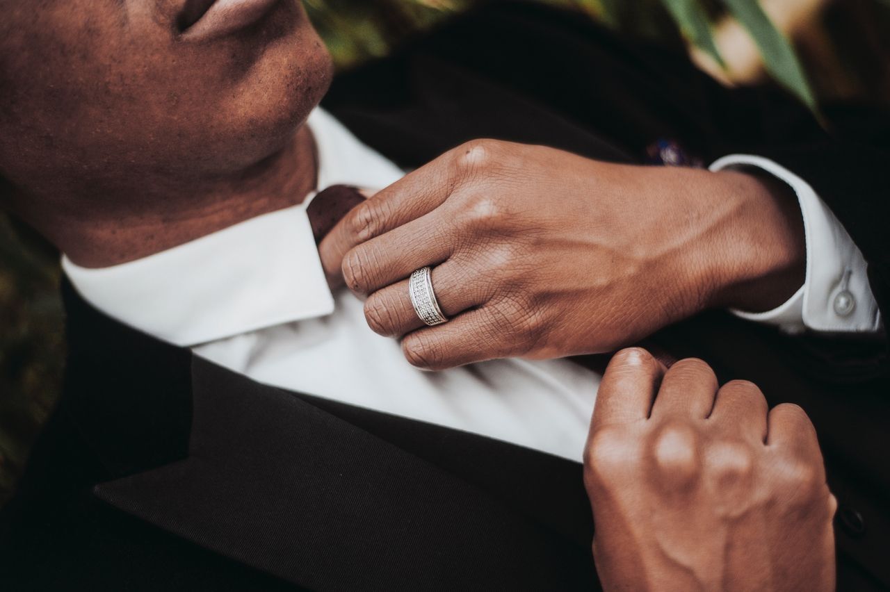 Close-up of a person in a suit adjusting his tie, highlighting a detailed silver ring on his finger. The mood is sophisticated and elegant. Close-up of a person in a suit adjusting his tie, highlighting a detailed silver ring on his finger. The mood is sophisticated and elegant.