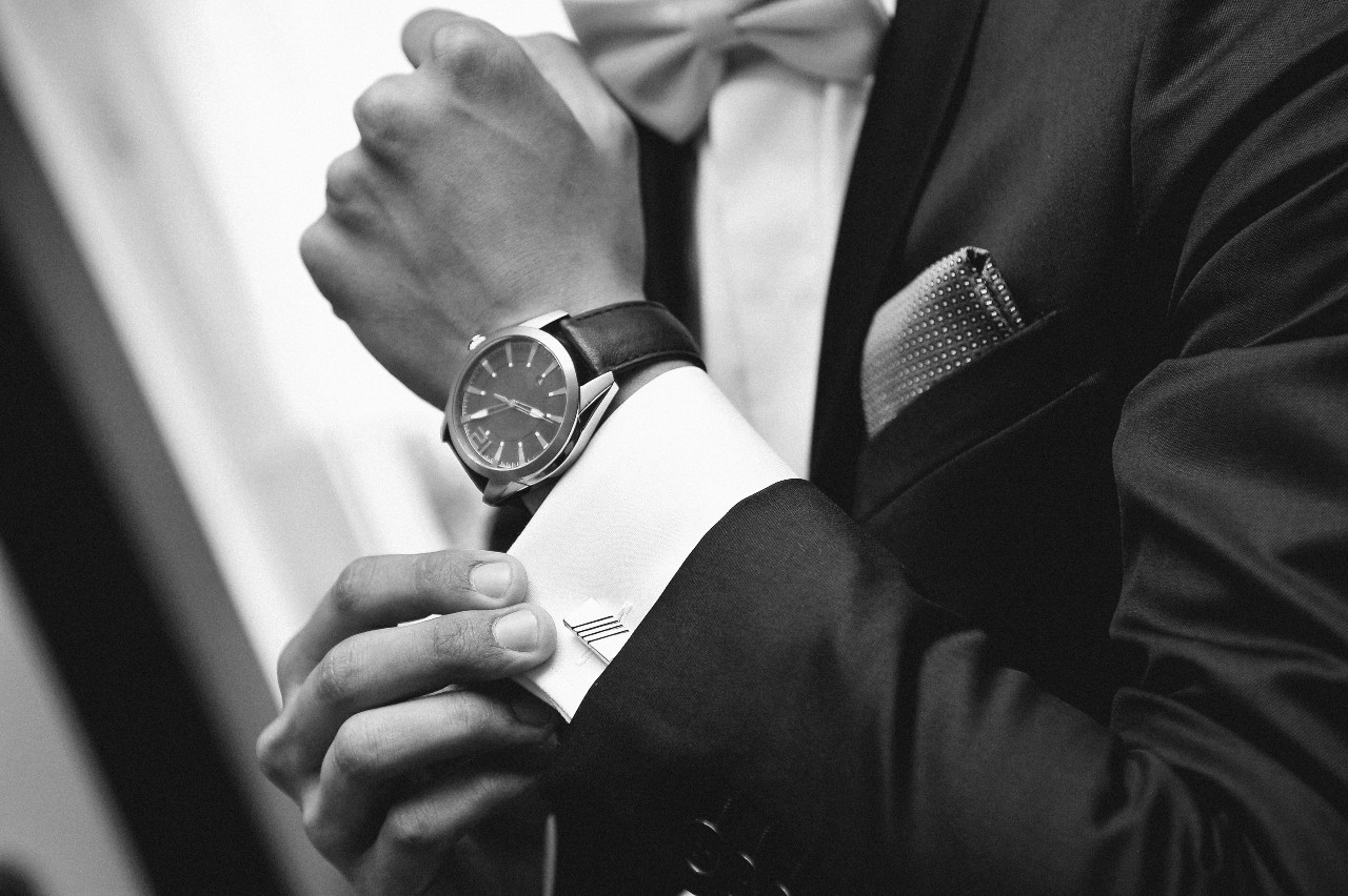 A black and white picture of a man in a suit fixing his cufflinks, showcasing his leather wristwatch. A black and white picture of a man in a suit fixing his cufflinks, showcasing his leather wristwatch.