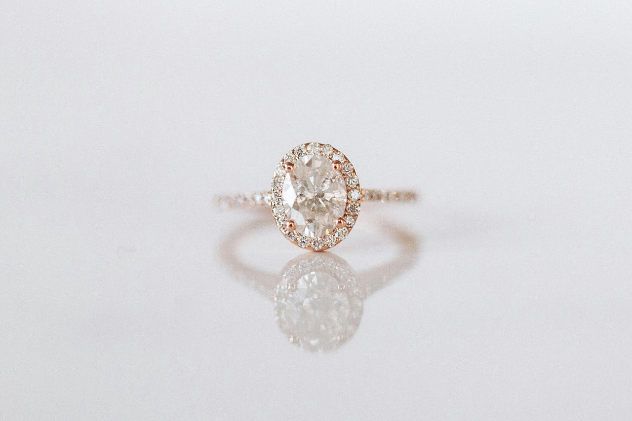 A rose gold halo engagement ring on a white reflective surface
