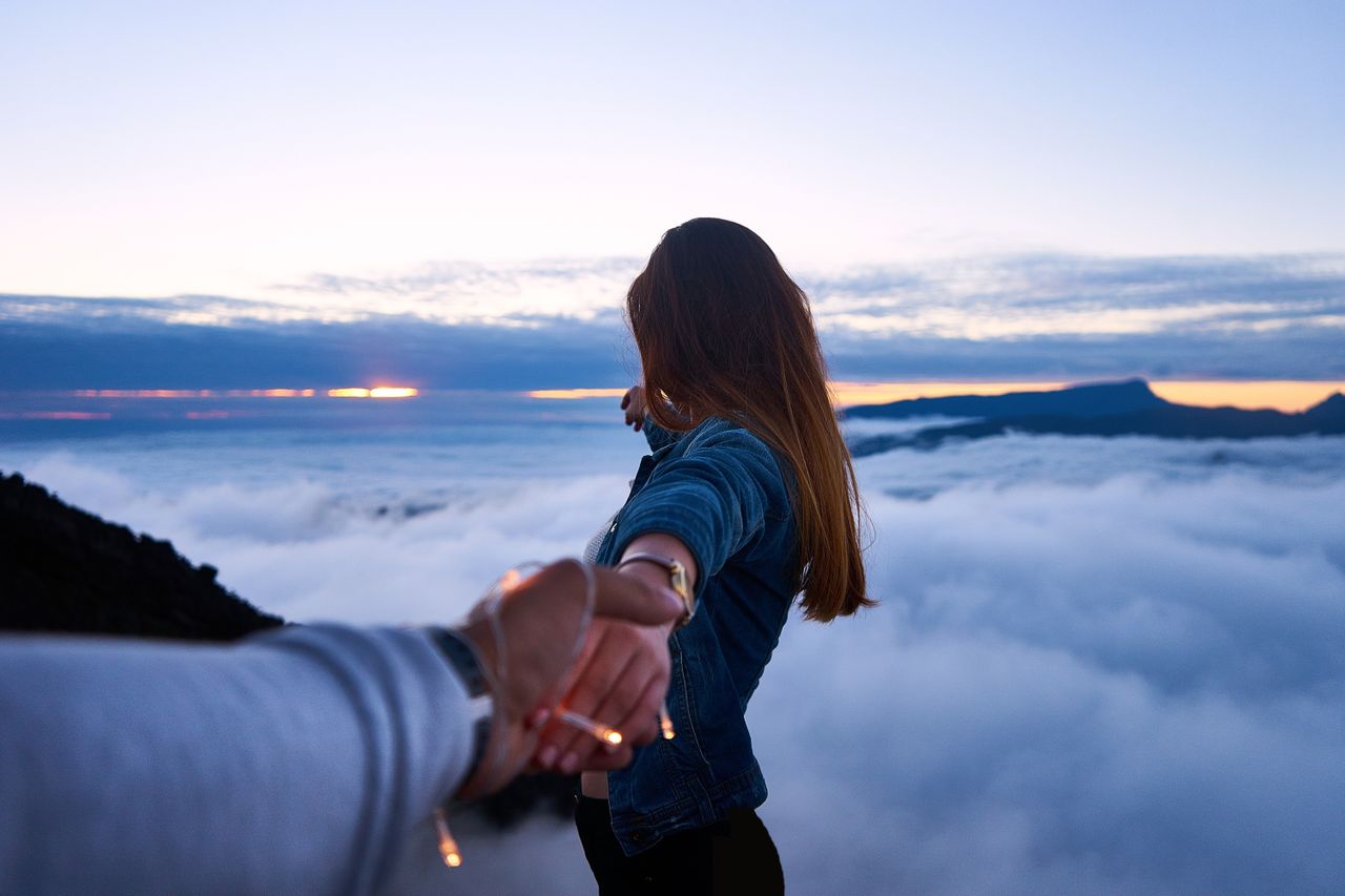 man and woman holding hands overlooking the clouds